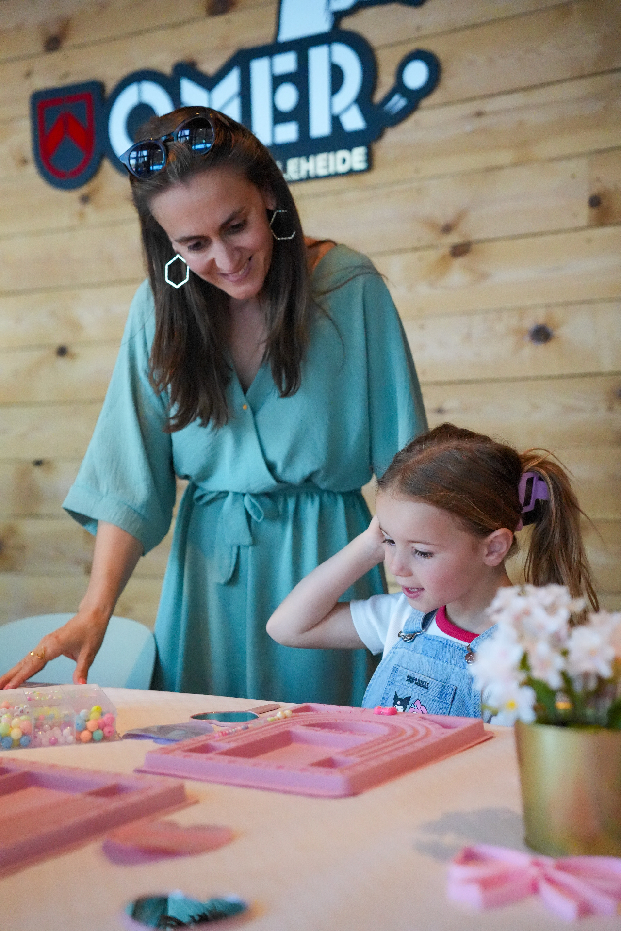 Laetitia van Atelier Kraal begeleidt een meisje aan tafel met kralen en een rijgplankje